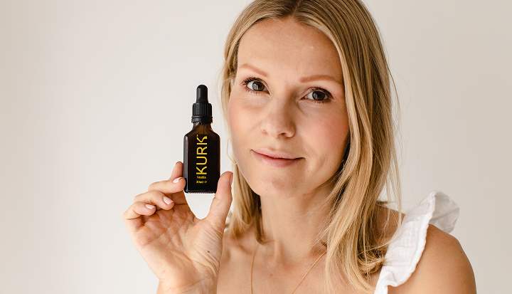 Woman holding a bottle of Kurks product against a plain background
